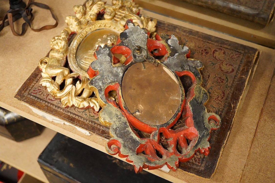 Two gilt metal plaques housed in giltwood ‘cherub’ frames and a heraldic leather folder with watered silk lining, 34 x 27cm